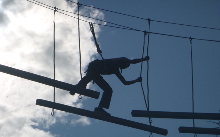the silhouette of a person navigating a ropes course